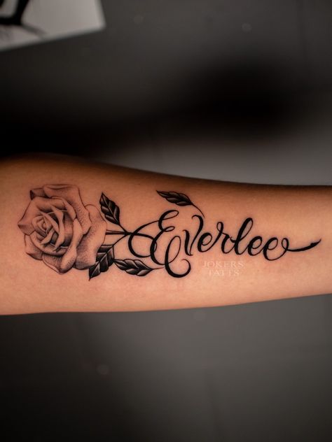 Flower Arm Tattoo With Name, Flower With Name Tattoo Ideas, Rose Tattoos With Names Stem, Name Tattoos With Rose, Rose And Name Tattoo Design, Name Tattoo Forearm Woman, Spouses Name Tattoo Ideas, Tattoo Ideas Of Names, Rose Name Stem Tattoo