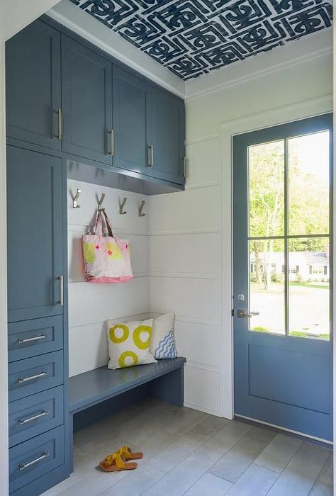 Black and white ceiling wallpaper complements a mudroom boasting blue cabinets donning nickel hardware while nickel hooks are fixed against a white paneled wall over a blue built-in bench. Shiplap Mudroom, Blue Mudroom, Mudroom Shelves, Blue Shiplap, Wallpaper On Ceiling, Mudroom Cabinetry, Blue Interior Doors, Transitional Laundry Room, Mudroom Cabinets