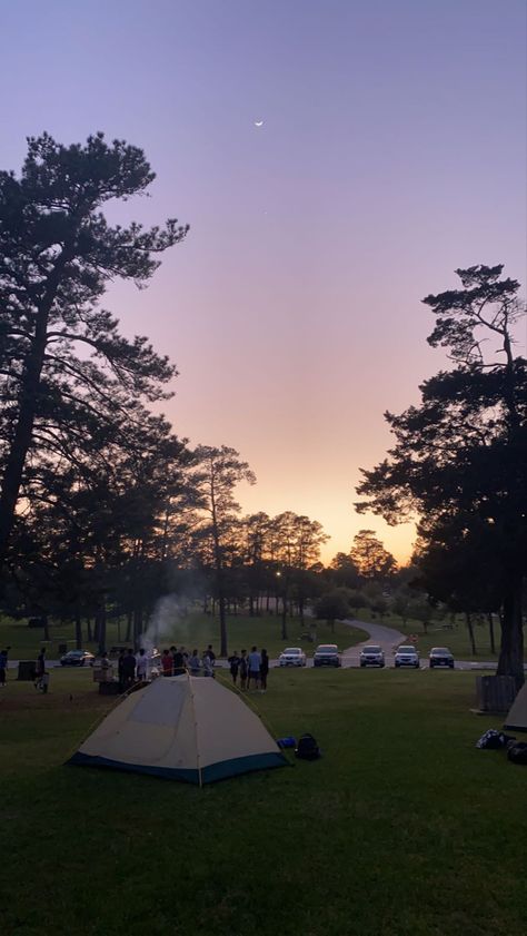 sunset view of some people camping in a nature park; there is a tent set up, trees, and white smoke coming up from a campfire Camping Aesthetic Friends, Sunset Nature Aesthetic, Tent Camp Set Up Ideas, Camping Background, Tent Camping Aesthetic, Camping Sunset, Nature Parks, Cool Camping Gadgets, Aesthetic Nature Photography