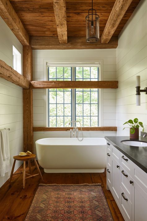 Cabin bathroom chunky wood beams and posts white shiplap in bathroom freestanding bathtub vintage bath mat double vanity stool in bathroom beam and window details exposed wood ceiling 2 light bath light wall sconce black counters | JAM Architecture Barn Bathroom, Cabin Renovation, Cabin Bathrooms, Barn Interior, Barn Renovation, Cabin Interiors, Modern Cabin, Wooden Beams, Cabin Design