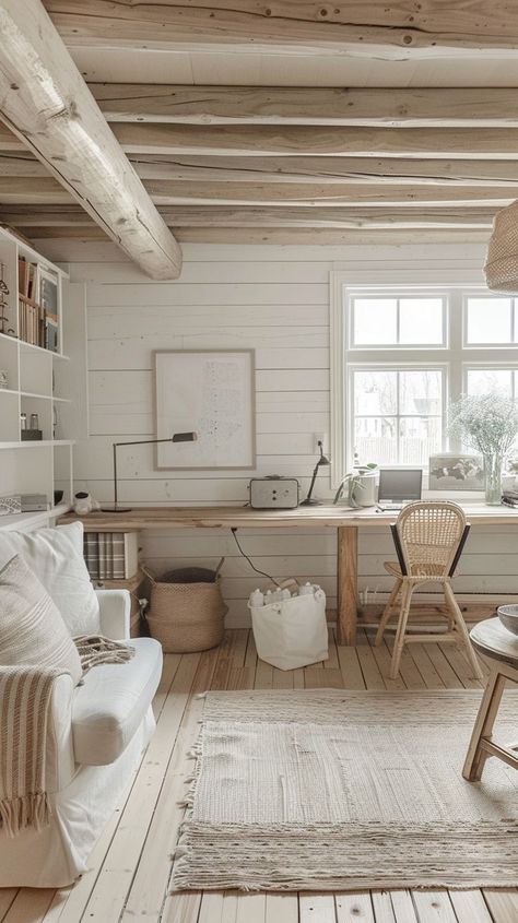 A cozy, light-filled cabin interior with a white couch, wooden ceiling beams, and a large window allowing natural light to fill the space. The decor includes a wooden desk with a wicker chair, a light beige rug, and various neutral-toned accessories. Scandinavian Cabin Interior, Cabin Interior Ideas, Cottage House Interior, Scandinavian Cabin, Scandinavian Cottage, Cottage Interior, Beige Interior, Cabin Interiors, Cabin Living