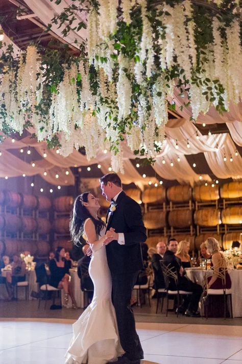 A large ceiling installation above the dance floor is a stunning focal point to a gorgeous white winter wedding. Filled with white flower and greenery hanging in an organic way the newly weds share a dance under the hanging flowers. Wedding Flower Ceiling Decor, Hanging Dance Floor Installation, Florals Hanging From Ceiling Wedding, Hanging Flower Installation Wedding, Ceiling Floral Decor, Hanging Floral Arrangements Wedding, Hanging Florals Wedding Reception, Wedding Ceiling Decorations Flowers, Flower Ceiling Wedding