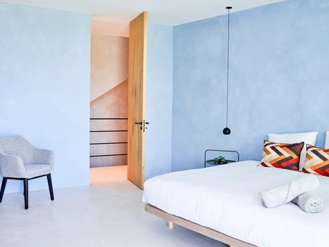 A minimalist bedroom with light blue limewash walls, a large white bed and a single blue chair. Blue Limewash, Modern Limewash, Bright Bedroom Colors, Limewash Walls, Airy Home, Nail Salon Interior Design, Bright Bedroom, Travel Nursery, Brighter Bedroom