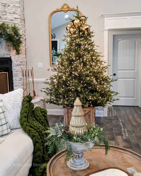 This living room features a round wood tray-top coffee table perched in front of an illuminated Christmas tree. The tree is placed inside a wooden box tree stand and topped with a gold jingle bell tree topper. Jingle Bell Tree, Unique Tree Toppers, Christmas Tree Decorating Ideas, Tree Decorating Ideas, Frosted Christmas Tree, Christmas Tree Decorating, Farmhouse Christmas Tree, Pencil Christmas Tree, Unique Christmas Trees