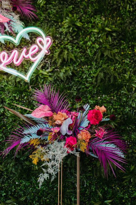 Colorful painted tropical florals against a greenery photo backdrop with Love neon sign. Design & Stationery @epitomepapers Planner @woodlandeventsmn Photographer @Empiriastudios Florals @WilderlandFloral Neon Signs | True Brilliance Co Venue | The Apt Neon Sign Wedding Backdrop Flowers, Tropical Floral Backdrop, Diy Neon Backdrop, Retro Tropical Party, Neon Tropical Wedding, Neon Wedding Flowers, Neon Floral Arrangements, Neon Flower Arrangements, Neon Disco Wedding