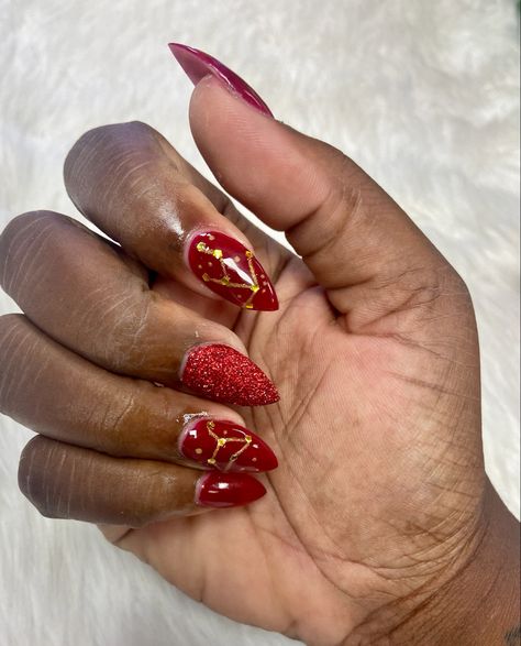 Subject is a medium brown skin hand over a white background. Hand bent with nails facing camera. Almond shaped medium length nails with cranberry red gel polish, one red glitter nail, and gold zodiac constellations. Constellations Leo and Taurus. Leo Nails Zodiac, Taurus Nails, Aries Nails, Zodiac Nails, Medium Length Nails, Red Gel Polish, Sagittarius Leo, Nail School, Taurus Pisces