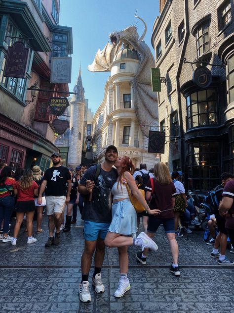 Photo of couple in front of gringotts bank at diagon alley in the wizarding world of harry potter at universal studios orlando. Both people hold a harry potter wand, girl is kissing boy on the cheek with a foot popped. Universal Studios Orlando Couple Photos, Universal Studios Couple Outfit, Couple Universal Studios, Universal Studios Outfit Couples, Universal Studios Photo Ideas Couple, Universal Couple Pictures, Universal Studios Couple Pictures, Harry Potter World Outfit Summer, Universal Studios Instagram Pictures