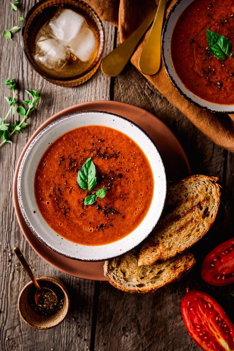 Overhead of Roasted tomato soup in a bowl topped with basil, pepper and served with grilled bread Soups Photography, Soup Pictures, Food Photography Styling Ideas, Soup Photos, Soup Photography Styling, Soup Photography, Tomato Soup Aesthetic, Soup Food Photography Styling, Tomato Soup Photography