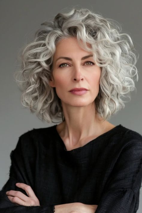 Elegant mature woman with curly gray hair and confident gaze, wearing a black top, arms crossed. Going Grey Transition Tips, Highlights For Grey Hair, Gray Curls, Grey Bob Hairstyles, Hair Color Guide, Grey Curly Hair, Womens Haircuts Medium, Going Grey, Grey Hair Inspiration