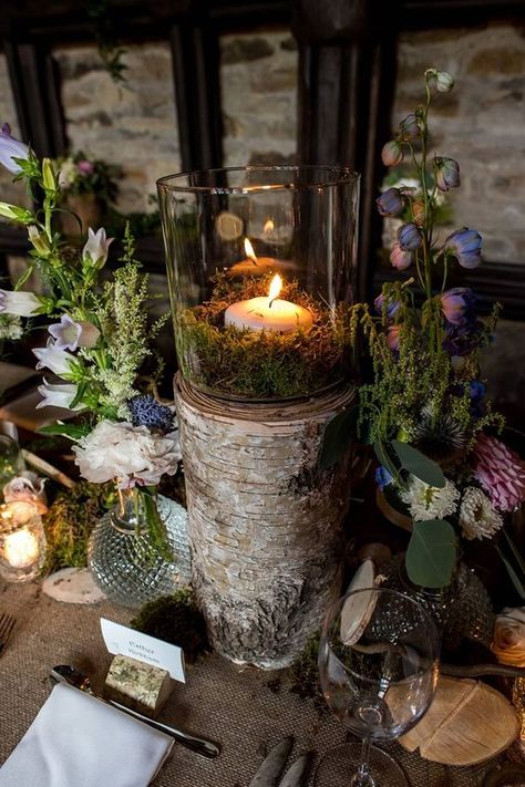 a woodland wedding centerpiece of bold blooms, greenery, moss and a tree stump with a candle and moss Green Moss Wedding Decor, Moss And Wood Table Decor, Moss And Roses Centerpieces, Small Enchanted Forest Wedding, Mossy Wedding Bouquet, Woodland Themed Wedding Decorations, Moss Party Decor, Spanish Moss Wedding Centerpiece, Moss Centrepiece