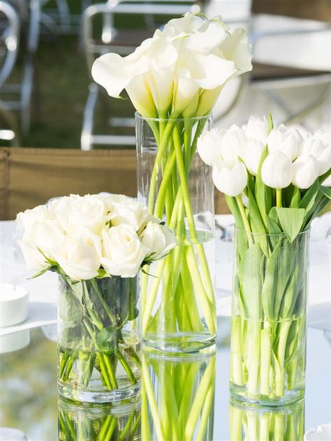 A trilogy of white roses, callas and tulips create a modern and minimalist wedding table decor | Athens Wedding Planner & Designer: @mitheoevents Photo: @JohnNassari Venue: @islandathens | #mitheoevents #weddingplannergreece #destinationweddingplanner #athenswedding #luxurywedding #iranianwedding #athensrivierawedding #weddingstyling #weddingdecor #allwhitewedding #tablesetting #tablescape #tabledecor #weddingflorals #whiteweddingflorals Floral Arrangements For Table, Tulip Centerpieces Wedding, Tulip Wedding Decorations, Tulip Table Decor, Chic White Wedding, Tulip Centerpiece, Black And White Wedding Theme, White Floral Arrangements, White Flower Arrangements