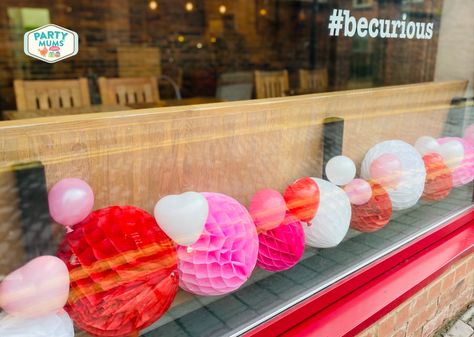 Honeycomb balls and heart shaped balloons add som ecolour to the cafe window. February Decor, Valentines Window Display, Church Valentines, Cute Window, Valentines Food Dinner, Valentines Party Food, Heart Shaped Balloons, Lounge Cafe, Cafe Window