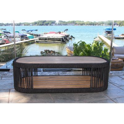 This coffee table completes your outdoor living room with a breezy, coastal aesthetic. Its distinct oval frame is crafted from solid teak wood with a lower shelf below the table top - great for drinks, snacks, and extra throw blankets. The design features black natural rope woven around the edges and on either end that gives it a dynamic look. We love that this coffee table has such a beach-y and organic vibe, but it's also resistant to water, UV rays, and rust. | Beachcrest Home Tena Outdoor Co Thanksgiving Mantel Decor, Outdoor Seating Set, Coastal Aesthetic, Outdoor Coffee Table, Teak Coffee Table, Outdoor Bar Stools, Outdoor Side Table, Sunbrella Cushions, Outdoor Living Room