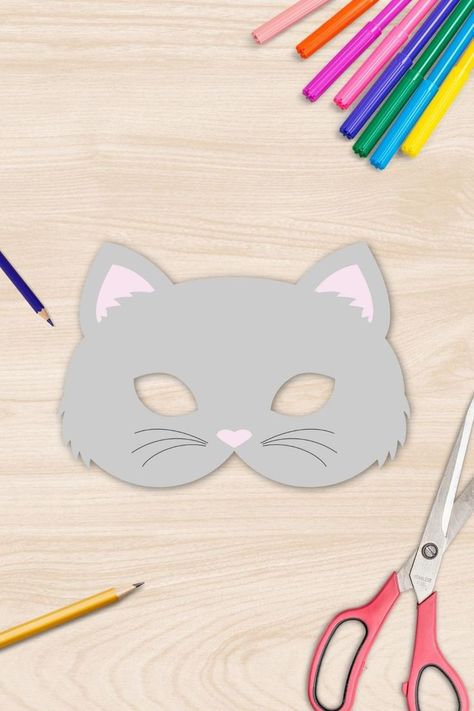 A cat mask made out of paper laying on a table surrounded by pens and scissors. Cat Mask Template, Cat Mask Template Free Printable, Cat Face Mask Diy, Cat Mask Printable, Cat Design Eye Mask For Costume, Halloween Cat Design Masks With Cat Ears, Cat Masquerade Mask, Cat Mask Diy, Cat Costume Diy