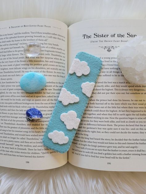 A light blue bookmark with white clouds sitting ontop of a book, surrounded by crystals. Foam Sheet Bookmarks, Gifts With Wool, Book Marks Felt, Easy Felt Patterns, Felt Bookmarks Handmade, Bookmark Clouds, Kids Bookmark Craft, Small Felt Projects, Diy Felt Bookmarks