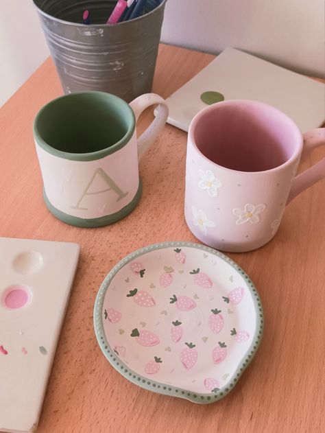 Pink and green pottery painting with flowers, strawberries and hearts, cute pottery painting ideas inspo, mugs spoon rests, jewellery dishes Green Pottery Painting, Spoon Rest Pottery Painting Ideas, Cute Pottery Painting, Cute Pottery Painting Ideas, Painting Pottery Ideas, Spoon Rest Pottery, Cute Pottery, Painting With Flowers, Clay Cafe