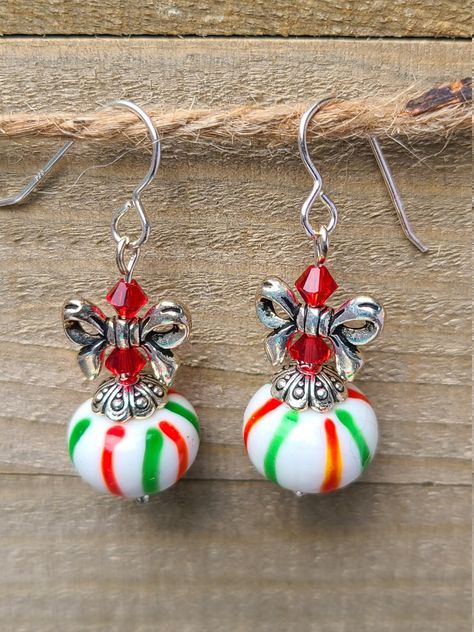 Red & Green Striped Ornament Beads with a Bow on top! Swarovski crystals, lampwork beads, and bows make up these earrings on Sterling Silver Ear Wires.  Lampwork Beads are handmade using a torch or lamp to melt the glass; when the glass has melted, the molten glass is rotated around a rod forming a base bead; then, swirls, dots, flowers, colors, and patterns are added to the base bead so that no two are exactly alike.  Bows (10x14mm) are antique silver-plated, lead-free pewter. Swarovski crystal Diy Christmas Earrings, Swarovski Ornaments, Xmas Jewelry, Diy Jewelry Charms, Head Display, Wire Ornaments, Wire Wrap Jewelry Designs, Sale Ideas, Chakra Beads