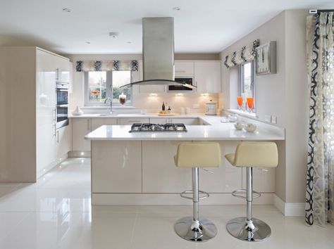 Sleek, modern minimalism informs the look of this kitchen, with expanses of glossy white in every direction. The large format tile flooring pairs well with white countertops and cabinetry, providing space for a pair of bar stools at the extended countertop in the foreground. Elegantly textured but transparent drapes add a healthy dose of visual complexity to the monolithic room. 14x14 Kitchen Layout, U Shaped Living Room, Kitchen Layout U Shaped, G Shaped Kitchen, Kitchen Design Images, Kitchen Layout Plans, Kitchen Design Color, Small Kitchen Layouts, Kitchen Modular