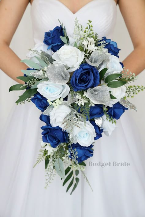 This lovely assortment of royal blue, light blue and white roses is bound to turn heads on your wedding day. This lovely cascading brides’ bouquet from the is an absolutely breathtaking arrangement for any bride to be, in any season. Sage greenery and silver sparkle calla lilies complete the look and add a delicate realism to this beautiful bouquet. This bouquet is 10” wide, 18” long, and is crafted by our in-house florists without using a foam base to anchor the flowers to the bouquet. Instead, Royal Blue Flower Arrangements, Royal Blue Wedding Bouquet Ideas, Wedding Ideas Royal Blue, Royal Blue And Light Blue Wedding, Silver Blue Wedding, Royal Blue Wedding Flowers, Wedding Blue And Silver, Blue White Wedding Bouquet, Ivory And Blue Wedding