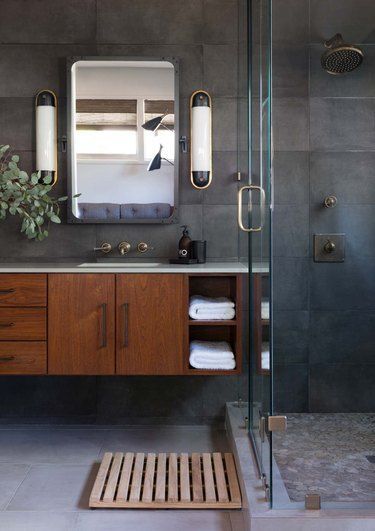 From exposed metal piping to concrete countertops, here are 20 industrial bathroom ideas worth stealing. #hunkerhome #industrialbathroom #industrialbathroomideas #industrial #industrialbathroominspo Windowless Bathroom Wallpaper, Charcoal Tile Bathroom, Mcm Bathroom Ideas, All Tile Bathroom, Mancave Bathroom, 1970s Bathroom, Round Table Design, Charcoal Bathroom, Bathroom Shower Stalls