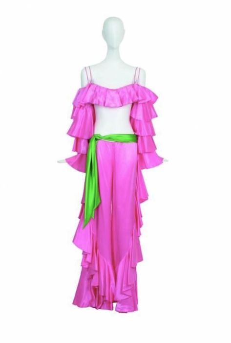 Worn on the February 14, 1973 episode of "The Sonny & Cher Comedy Hour" during Cher's performance of "It Never Rains In Southern California." Hot pink satin top and pants with ruffled sleeves and legs, (illustrated with subsequently added green sash) designed by Bob Mackie. Cher recalled that "We laughed so hard while we were shooting this concert part of Sonny and Cher, cause Son didn't learn the song, so I taught it to him on the spot and he kept laughing and blowing the words." Cher Butterfly Outfit, Cher Yellow Outfit, Hot Pink Satin Top, Cher If I Could Turn Back Time Costume, Cher Halloween Costume Singer, Pink Satin Top, If I Could Turn Back Time Cher, Green Sash, Sonny Cher