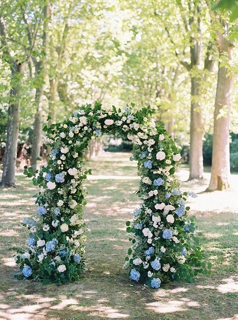 shades of blue destination wedding color combos for 2024, white bridal gown, mismatched bridesmaid dresses in dusty blue, sky blue and ice blue, dusty blue and white flower and greenery wedding arch and escort display decor, dusty blue wedding tablecloth, sky blue wedding invitation covers, wedding favors basket with light blue ribbons. Shades Of Blue Bridal Party, Blue And White Fall Wedding, Green And Blue Wedding Theme, Spring Blue Wedding, Blue And Green Wedding Theme, Mismatched Blue Bridesmaid Dresses, Blue Destination Wedding, Greenery Wedding Arch, Sky Blue Wedding