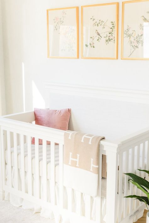 This crib has a neutral linen upholstered panel, which brings a softness to the space. The gold frames above the crib look so good agaist the white and creamy tones. Nursery With Gold Accents, Neutral Nursery Design, White Nursery Furniture, Nursery Design Neutral, Nursery Interior Design, Nursery Interior, Kids Interior Design, Gold Nursery, Glider And Ottoman