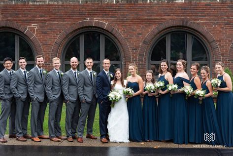 Groomsmen wearing gray suits and bridesmaids in navy dresses. Navy And Grey Wedding Colors, Navy Bridesmaids And Grey Groomsmen, Navy And Gray Wedding Party, Navy Blue Bridesmaids And Groomsmen, Navy Groomsmen Suits And Bridesmaids, Navy Bridesmaids And Groomsmen, Dark Grey Groomsmen Suits, Navy Blue And Grey Wedding, Groomsmen Attire Navy Blue