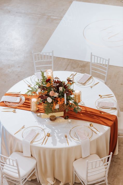 Main wedding table with burnt orange table runner. Decorated with a floral centerpiece alongside candles and furnished with glassware. Wedding Decor Terracotta, Terracotta Wedding Bridesmaid Dresses, Orange Dress Outfit Wedding, Burnt Orange Table Runner, Bridesmaid Dresses Burnt Orange, Copper Saree, Burnt Orange Wedding Theme, Orange Dress Outfit, Orange Wedding Decorations