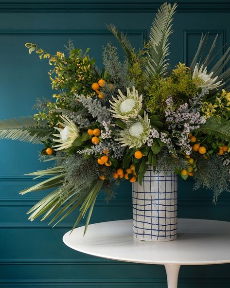 Mediterranean palms, cypress, berried euonymus, queen protea, fruiting citrus, gray kochia spears, and pink statice. Paula Greif hand-painted grid vase, for information: paulagreifceramics.com Holiday Flower Arrangements, Winter Flower Arrangements, Winter Floral Arrangements, Winter Arrangements, Large Flower Arrangements, Corporate Flowers, Christmas Flower Arrangements, Flower Vase Arrangements, Modern Flower Arrangements