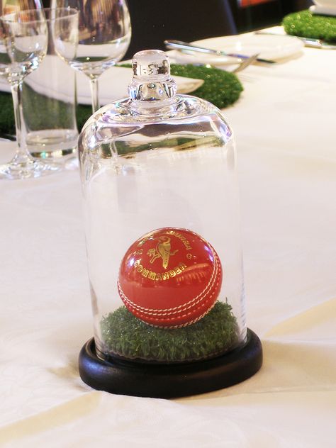 A Cricket Ball on a round of turf in a Cloche Cricket Centerpiece Ideas, Cricket Party Decorations, Cricket Party, Rugby Party, Sports Themed Wedding, Birthday Party Table Decorations, Cricket Ball, Hockey Table, Dad Birthday Cakes