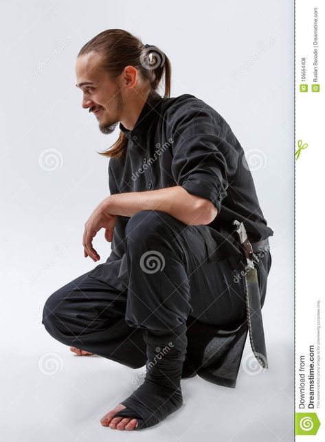 Photo about Ninja young with a beard in black uniform and a grin sat on one knee close-up on a gray background. Image of caucasian, background, dark - 105554408 Guy Kneeling Pose, Sitting On Knees Pose Reference, Kneeling On One Knee Pose Reference, Sitting Knees Up Reference, Sitting With Knees Up Pose, Guy Kneeling, Down On One Knee, Black Uniform, Background Dark