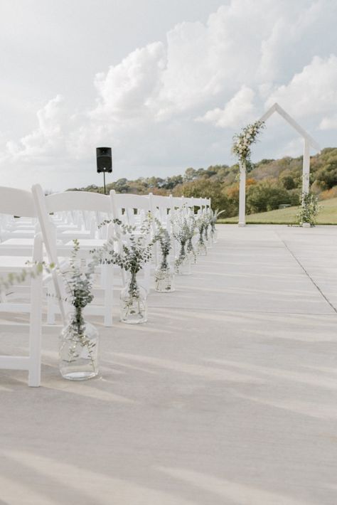 Ceremony floral installation on white arbor with textural white and neutral flowers and greenery. Clear glass jugs with greenery lining the ceremony aisle Flower Vases Down Aisle, Glass Jugs Wedding Aisle, Wedding Isles Decoration Chapel, Glass Jug Wedding Aisle, Carboys Wedding, Eucalyptus Wedding Ceremony Aisle, Isle Ceremony Decorations, Wedding Aisle Flower Vases, Floral Arrangements Down The Aisle