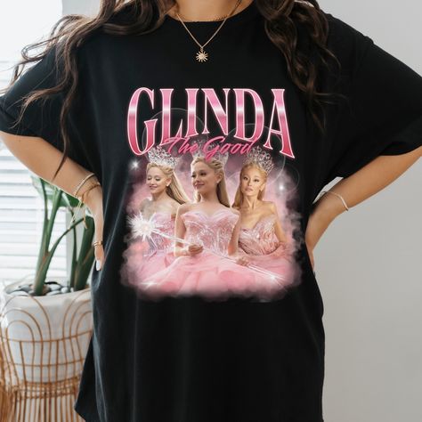 "Vintage 90s bootleg t-shirt featuring Ariana Grande as Glinda from Wicked. This unique design showcases a whimsical illustration of Glinda with vibrant colors and playful text, perfect for musical theater fans and collectors. Ideal for casual wear or as a standout piece in any wardrobe. Shop now for a touch of Broadway nostalgia! Glinda Popular, Ariana Grande Vintage, Wicked Ariana Grande, Wicked Merch, Glinda Wicked, Glinda The Good, Merch Shirt, Glinda The Good Witch, Good Witch