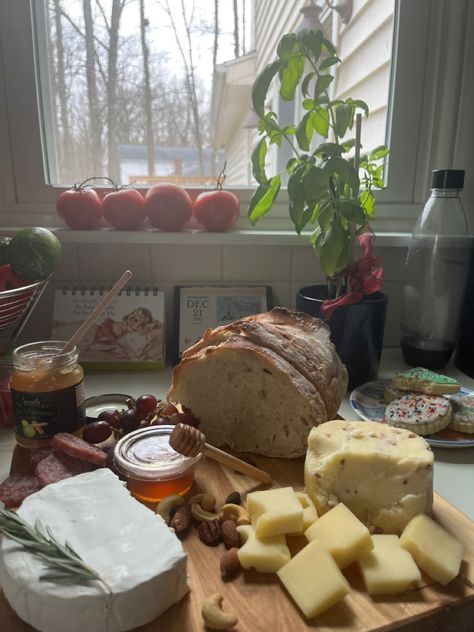 Photo of a grazing board on a white counter with red grapes, a loaf of bread, and cheese in a wheel with a rosemary garnish and cubed cheeses with nuts and honey near. There are herbs on the counter. Cheese Astetic, Cheese Making Aesthetic, Cottagecore Life Aesthetic, Crunchy Mom Aesthetic, Cheese Board Aesthetic, Cute Aesthetic Food, Cottagecore Thanksgiving, Crunchy Aesthetic, Cheese Aesthetic