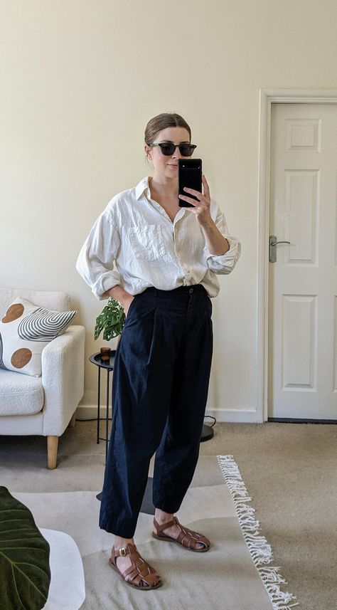 A woman stands in front of a mirror. She wears green sunglasses, a white linen shirt open at the collar, cropped navy trousers and brown fisherman sandals. Navy Sandals Outfit, Outfit With Linen Shirt, Brown Fisherman Sandals Outfit, Barrel Trousers Outfit, Brown Leather Sandals Outfit, Fisherman Outfit Aesthetic, Fisherman Outfits, Fisherman Aesthetic Outfit, Art Class Outfit