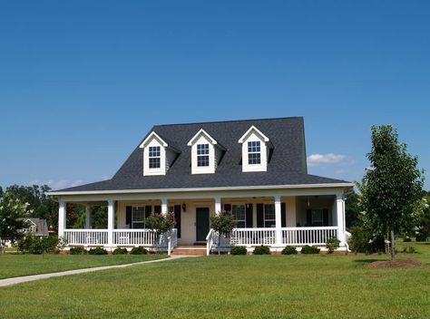 White farmhouse with wrap-around porch and dark gray roof with three white dormer windows prominently jutting out from the long sloping roof. House With Dormers, Dormer House, Dormer Roof, Big Porch, Black Roof, Cape Cod Style House, Foreclosed Homes, Suburban House, Dormer Windows