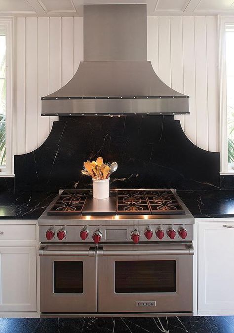 Black and white kitchen features white shaker cabinets paired with black soapstone countertops and backsplash. Cooktop Backsplash, Black Kitchen Backsplash, Herringbone Tile Backsplash, Green Kitchen Island, Transitional Kitchen Design, Black Backsplash, White Shaker Kitchen, Soapstone Countertops, Outdoor Kitchen Appliances