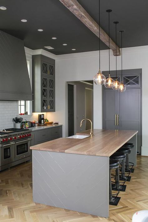 Gray kitchen features four glass pendants illuminating a gray herringbone center island topped with honey stained wood countertops fitted with a sink and brass gooseneck faucet lined with backless industrial bar stools placed atop a light wood herringbone wood floor. Dark Ceiling Light Walls, Rustic Kitchen Ideas, Herringbone Kitchen, Contemporary Style Kitchen, Dark Ceiling, Off White Kitchens, Herringbone Wood Floor, Herringbone Wood, Wood Floor Kitchen