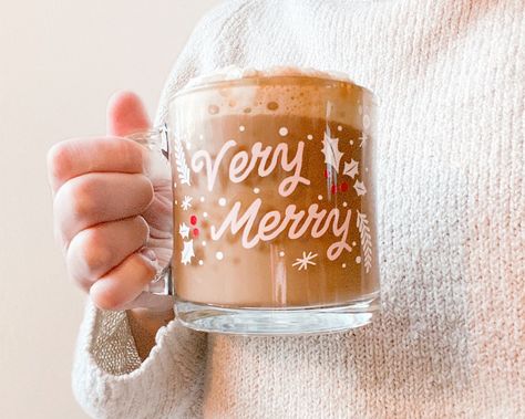 Cozy up by the Christmas tree and enjoy the essence of the holiday season with your favorite festive coffee or hot chocolate! Very Merry Clear Glass mug has a vinyl design hand applied. Festive Christmas mug is the perfect holiday gift!13 oz. clear glass mug with vinyl design applied. Made to order. While the vinyl adhesive is permanent, these mugs are hand wash only. Do not microwave. *Due to the handmade nature of this product, products may vary slightly. Holiday Mugs Diy, Coffee Vinyl Ideas, Clear Mug Cricut Ideas, Cricket Vinyl Ideas, Christmas Glass Mugs, Holiday Mugs Cricut, Vinyl Christmas Mugs, Christmas Glass Cup Ideas, Cricut Christmas Mug Ideas