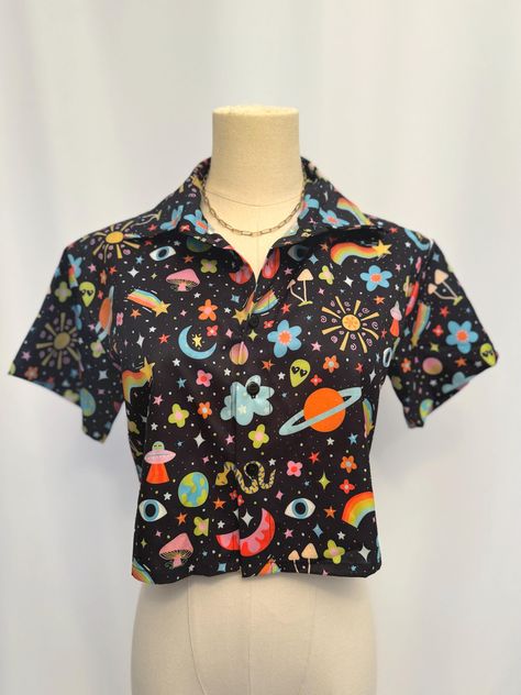 This eye-catching, 4-way stretch shirt is a vibrant and whimsical statement piece that effortlessly blends retro and space-age vibes. The shirt features a playful, colorful pattern set against a black background. The design showcases an eclectic mix of planets, rainbows, flowers, mushrooms, stars, and cosmic symbols, creating a mesmerizing and fun galaxy-inspired print. The shirt has a cropped silhouette with a classic collared neckline and short sleeves, making it perfect for those who love to stand out with a unique style. The button-up front allows for versatile styling, whether you're pairing it with high-waisted jeans for a casual day out or layering it over a dress for a quirky twist. Whether you're a fan of retro fashion, love cosmic themes, or just want to add some fun to your ward Cosmic Symbols, Crop Top With Collar, Space Babe, Rainbow Festival, Button Down Crop Top, Silly Clothes, Top With Collar, Stars Moon, Funky Outfits