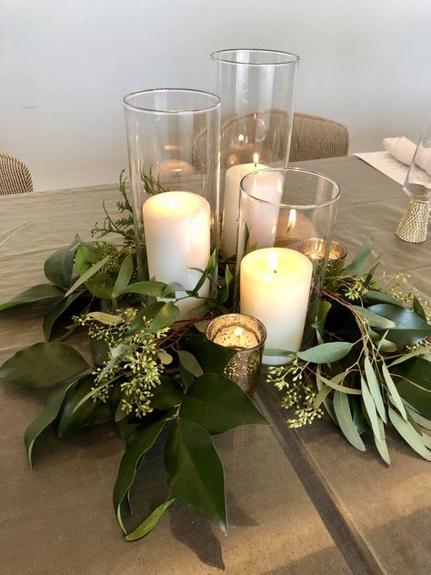 This pillar candle trio, gold mercury glass votives, and various kinds of greenery make up this table's centerpiece. Votives And Greenery Centerpiece, Gold Candle Holder Decor, Greenery And Candle Centerpiece, Candle Trio Centerpiece, Evergreen Candle Centerpiece, Fern And Candle Centerpiece, Pillar Candle Centerpiece, Glass Candle Centerpieces, Centerpiece Greenery