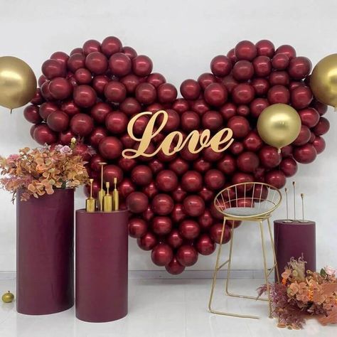 Set the perfect romantic backdrop for your special event by clustering burgundy balloons together in a heart shape. Place a ‘Love’ sign in the center as the focal point of the backdrop while accenting it with classy gold balloons to add some glimmer. Place an arrangement of orchids, roses, and chrysanthemums atop a burgundy column stand & on the floor for added texture while completing the look by placing some sleek gold candle holders atop pedestal pillars for added visual appeal. Burgundy Balloons Decoration, Heart Shaped Balloon Garland, Heart Balloon Garland, Wine Colored Wedding, Just Married Banner, Rose Gold Party Decor, Valentines Balloons, Gold Candle Holders, Wedding Planning Decor