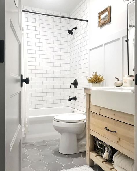 White tub and shower combo clad in white subway tile is fitted with a black faucet kit. A white toilet in front of the shower stands next to a light wood washstand in this gray hexagon floor tile bathroom. Tile Above Sink Bathroom, Hexagon Tile Bathroom Floor, Grey Bathroom Floor, Hexagon Tile Bathroom, White Subway Tile Shower, White Subway Tile Bathroom, Hexagon Tile Floor, Subway Tile Showers, Grey Bathroom Tiles