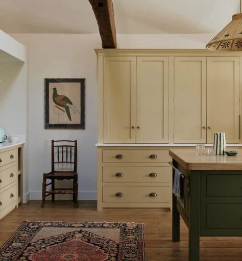 Kitchen with navy blue island in front on wooden floor with floor to ceiling cupboards on the back wall in buttery yellow with brass handles. To the right is a vintage wooden chair with old art work above. Wooden Island Kitchen, Warm Kitchen Ideas, Old Art Work, Vintage Yellow Kitchen, Vintage Wooden Chair, Cottage Core Home, Colonial Kitchen, Kitchen Storage Solutions, Floor To Ceiling