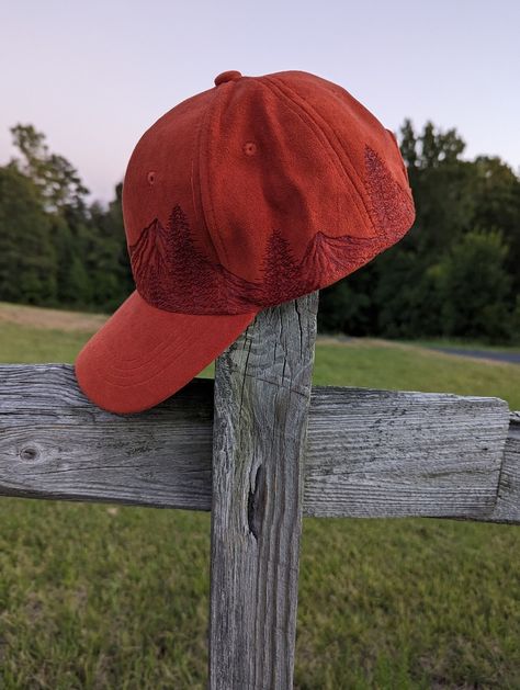 This handburnt orange baseball hat would make a great addition to your fall wardrobe. #burntballcap #orangebaseballhat #orangebaseballcap #mensballcap #mensfallfashion #autumnvibes #woodsy #forestcorefashion #hikinghat #fauxsuedehat #naturelovergift #landscapecap #casualstyle #mountainhat #pinetree #woodburnedhats Burned Ball Cap, Burned Baseball Hat, Forestcore Fashion, Fall Baseball, Mountain Hat, Hiking Hat, Hand Burn, Red Cap, Mens Fashion Fall