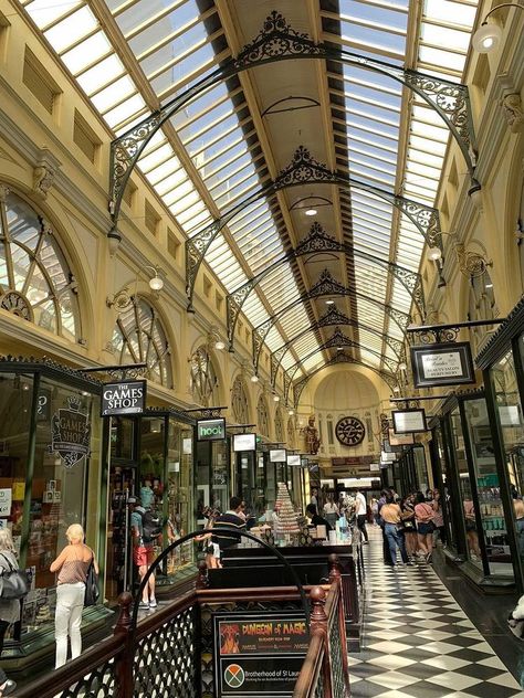 A cream painted hallway lined with shops. The roof is tall and arched and there are black cast iron details such as spandrels and shop signs. Two felling windows shine down revealing the clock and two statues at the end of the hall. Dark Academia Shopping, Shopping Arcade, Mall Design, Melbourne Australia, Dark Academia, Design Interior, Melbourne, Bucket List, Places To Visit