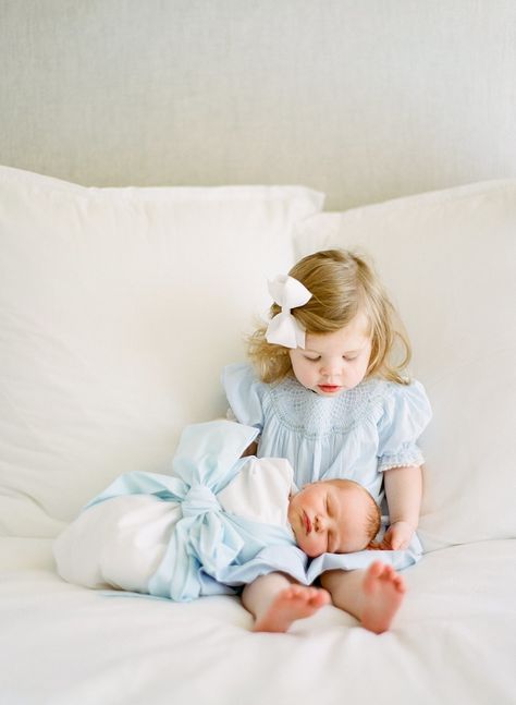 Image of a toddler wearing a blue dress, sitting on a bed with her newborn baby brother laying on her lap. He's wrapped in a blue bow swaddle. Blue And White Newborn Family Pictures, 2 Under 2 Newborn Pictures, New Sibling Photoshoot, Newborn Boy Photography With Siblings, Newborn Photos With Sister, Newborn With Toddler Photography, Newborn With Sister Photography, Newborn Photos With Big Sister, Newborn Toddler Family Photos