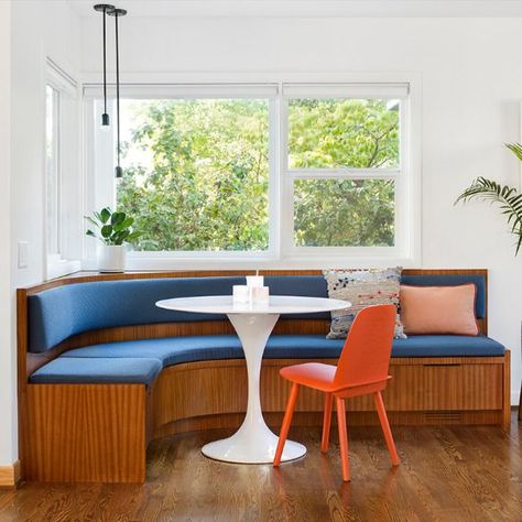 A rounded built-in banquette dining nook in Portland, Oregon with vertical grain stripes along the bottom, custom blue upholstered cushioning on the seats and back which wrap around the entire build.  A persimmon-colored chair is seated at a modern white rounded dining table, and black corded light fixtures hang above the banquette.  Part of a kitchen and dining interior design remodel by Dyer Studio. Mid Century Banquette, Modern Banquette, Seating In Kitchen, Banquette Seating In Kitchen, Banquet Seating, Modern Remodel, Kitchen Banquette, Booth Seating, Built In Seating