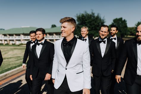 White Tux Black Shirt, Groom Suit White And Black, White Tux Black Pants, Groom White Jacket Black Pants, White Tux Groom With Groomsmen, White Tux For Groom, White Tux Black Pants Groom, Black And White Wedding Bride And Groom, White Tux Groom